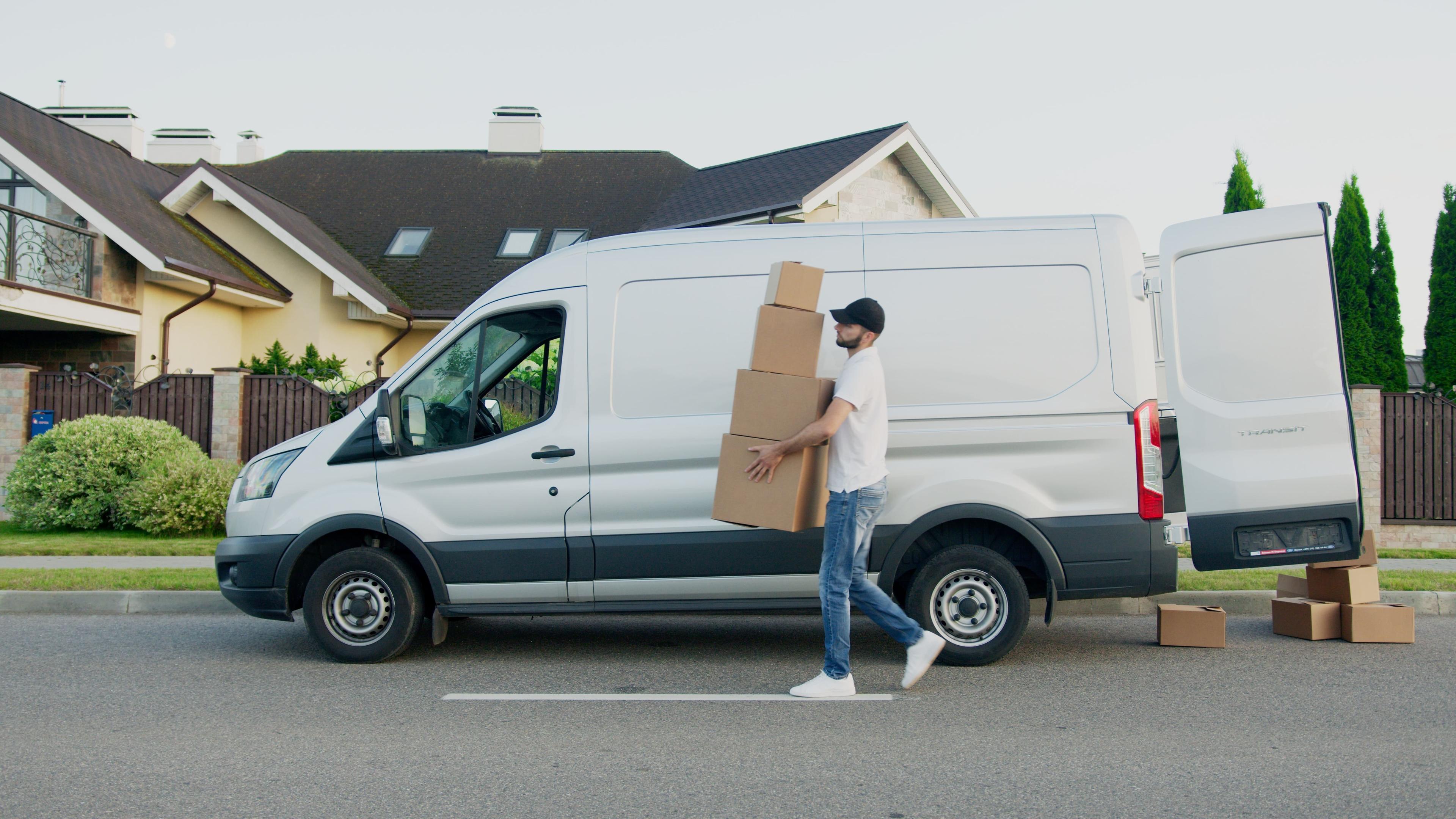 A delivery driver walking in front of a delivery van carries four packages to a customer's door